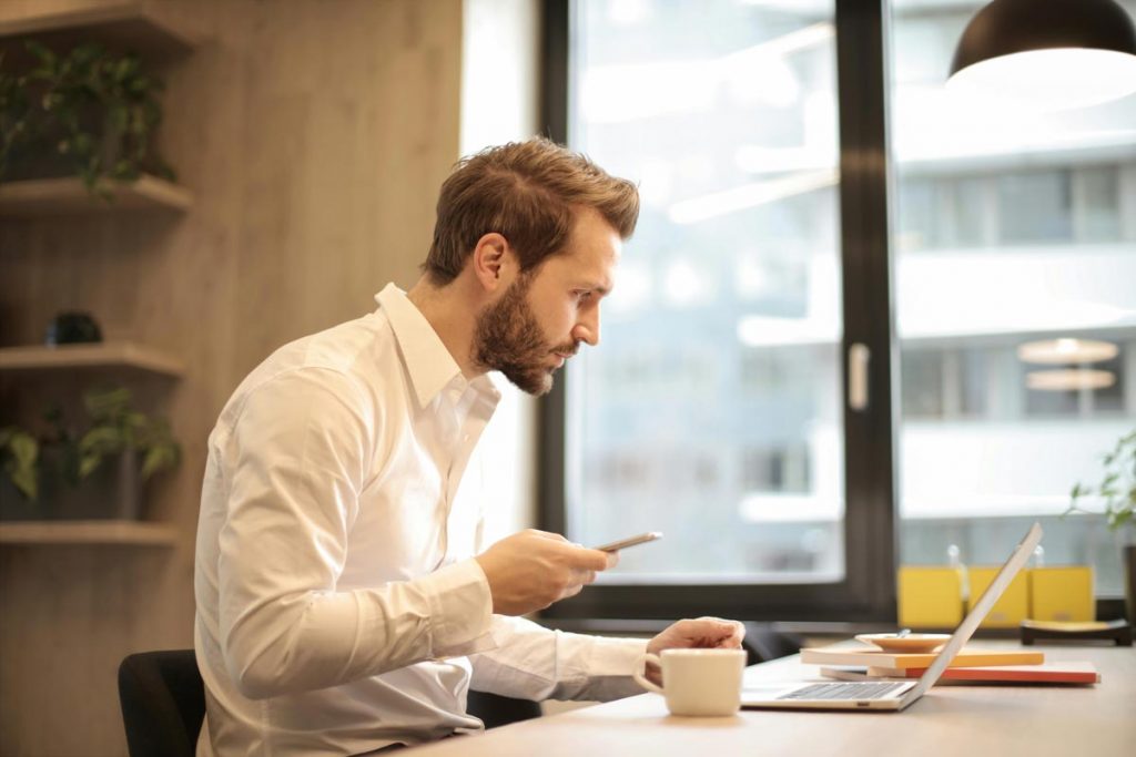 Man In White Shirt Using A Phone And A Computer